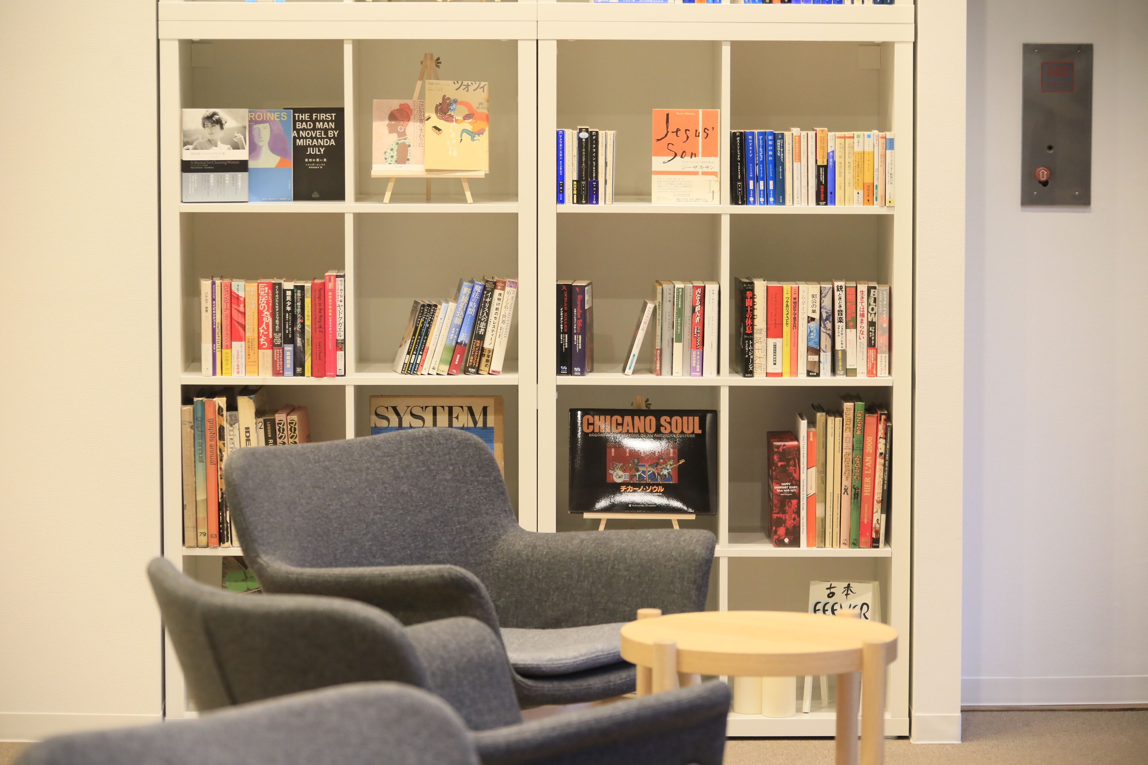 Una biblioteca con estanterías, un sillón gris y una pequeña mesa de madera.