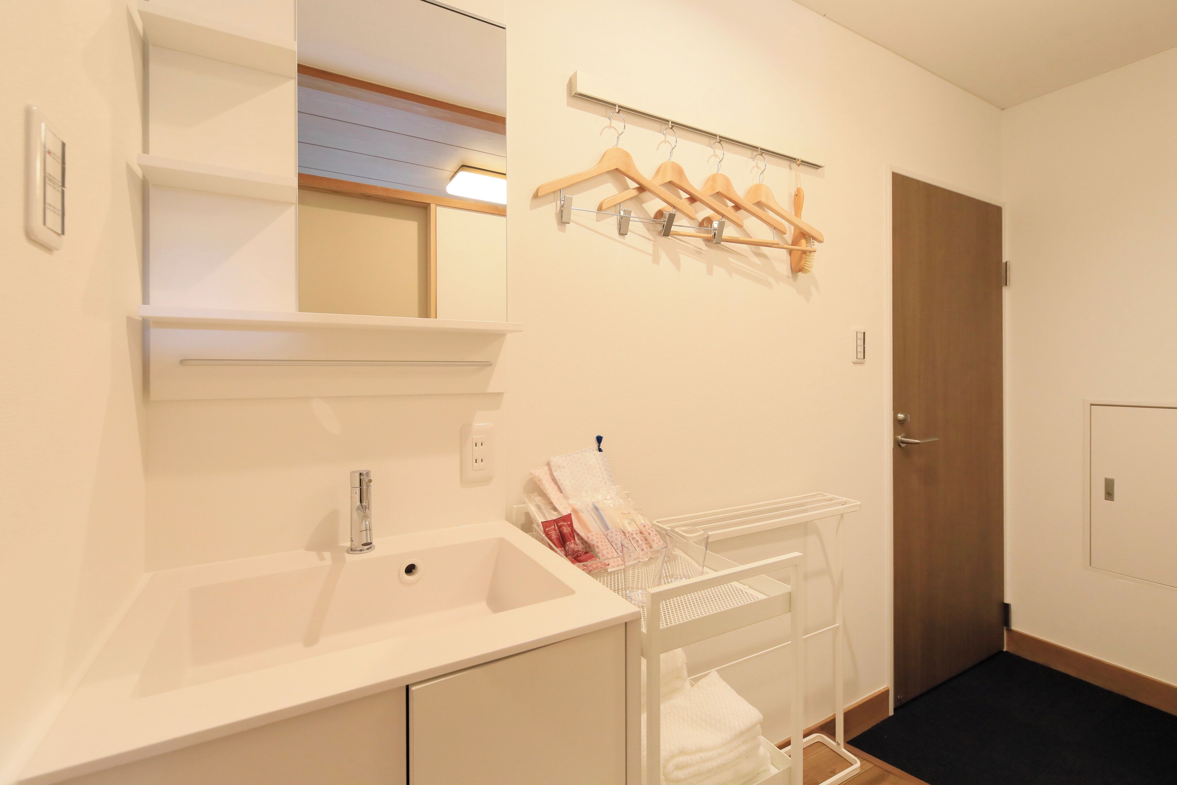 Une salle de bain avec un lavabo, un miroir, un porte-manteau en bois et une porte.