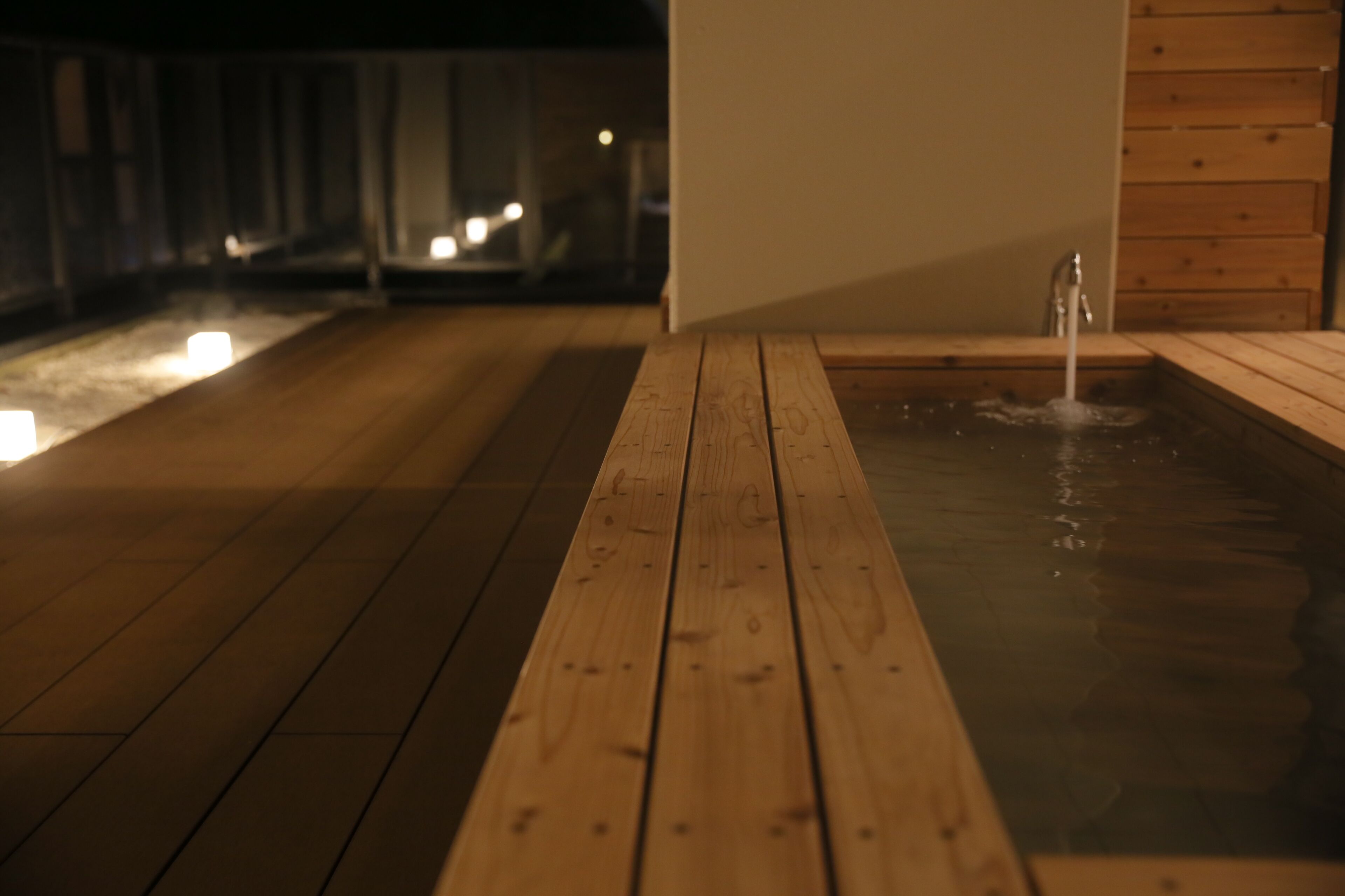 A wooden deck leading to a hot spring with a wooden wall and a wooden bench.
