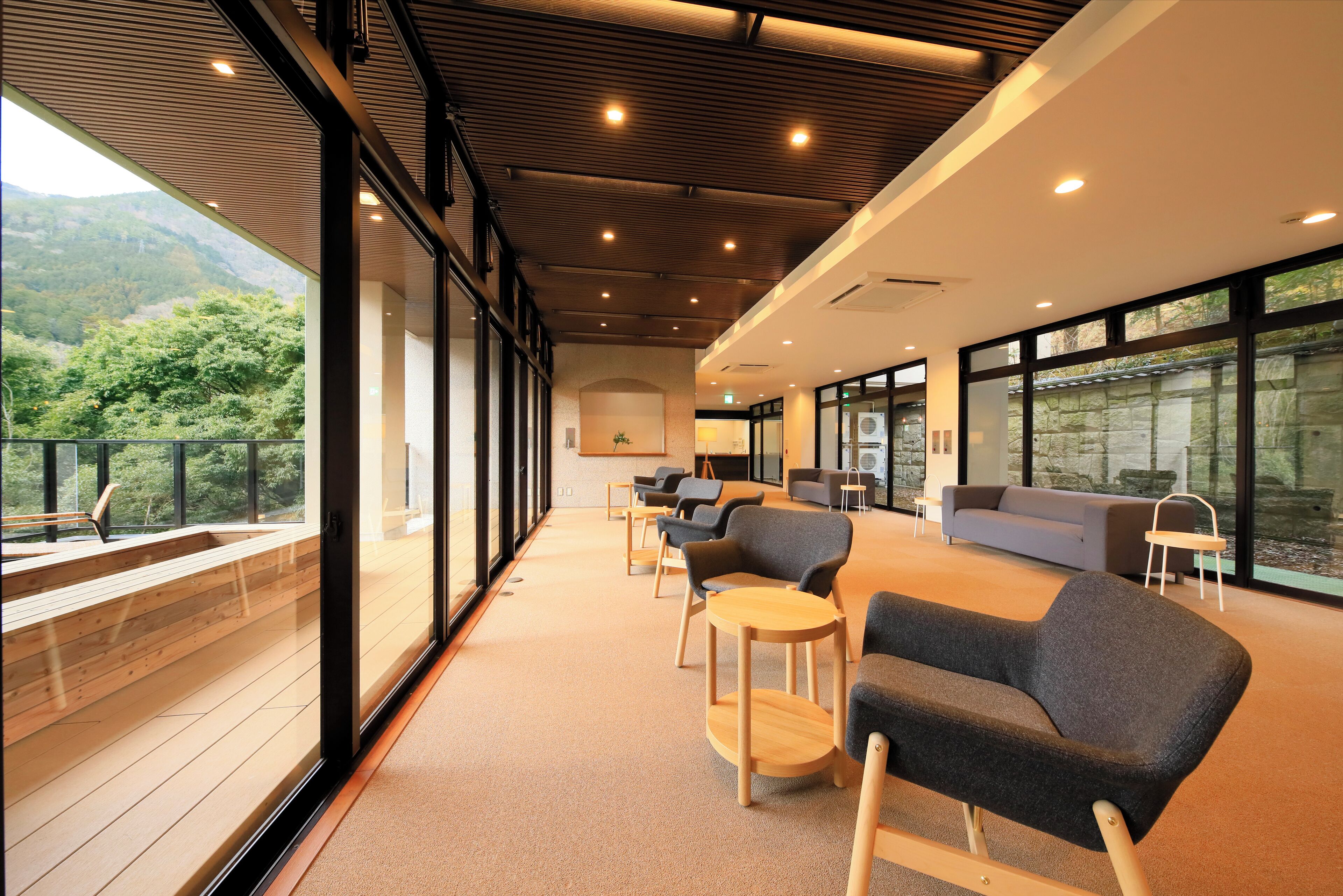 A spacious indoor area with large windows, wooden flooring, and modern furniture.