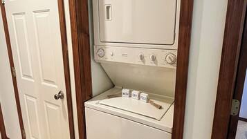 A compact, wall-mounted washer and dryer unit with a wooden frame, a control panel with dials, and a small shelf with a jar.