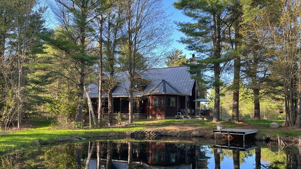Une cabane avec un étang devant, entourée d’arbres.
