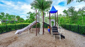 A playground with a slide, climbing structure, and a blue-roofed playhouse. - Indulge in a lavish home, heated saltwater pool, & spa, near all Naples offers. (Naples)