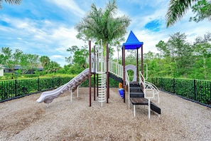 Ein Spielplatz mit Rutsche, Klettergerüst und einem Spielhäuschen mit blauem Dach.