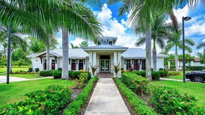 A two-story house with a central entrance, surrounded by well-maintained gardens and palm trees. - Indulge in a lavish home, heated saltwater pool, & spa, near all Naples offers. (Naples)
