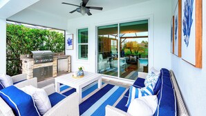 An outdoor patio with a grill, seating area, and a ceiling fan. - Indulge in a lavish home, heated saltwater pool, & spa, near all Naples offers. (Naples)