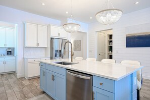 Una cocina moderna con una isla central, electrodomésticos de acero inoxidable e iluminación colgante.