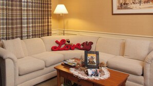 A living room with a beige sofa, a wooden coffee table with a photo frame, a lamp, and a plaid curtain.