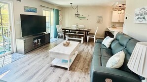 A spacious living room with a ceiling fan, a TV, a dining table, and a sofa. - Short walk to ocean and sound! NEW HOT TUB, FREE use of golf cart! Several decks (Emerald Isle)