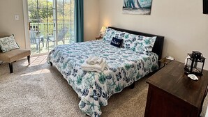 A bedroom with a large bed, a ceiling fan, a painting, a desk, and a view through a window. - Short walk to ocean and sound! NEW HOT TUB, FREE use of golf cart! Several decks (Emerald Isle)