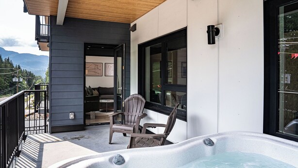A modern outdoor seating area with a hot tub, wooden chairs, and a view of mountains.