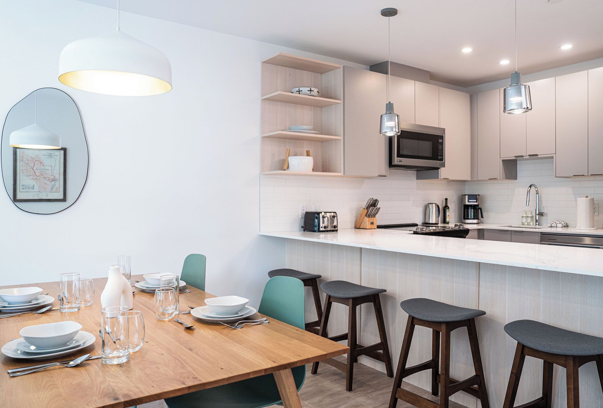 A modern kitchen with white cabinets, a wooden dining table, and bar stools.