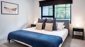 A bedroom with a bed, two bedside tables, a window with a view, and a framed picture on the wall.