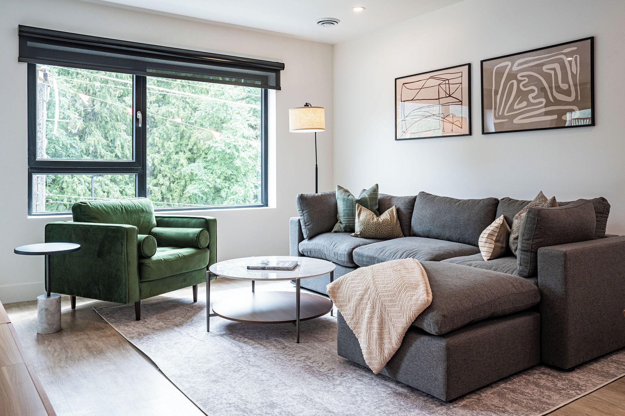 Un salon moderne avec un fauteuil vert, un canapé gris et une table basse ronde.