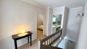 A hallway with a desk, a bed, and a bathroom with a mirror and sink.
