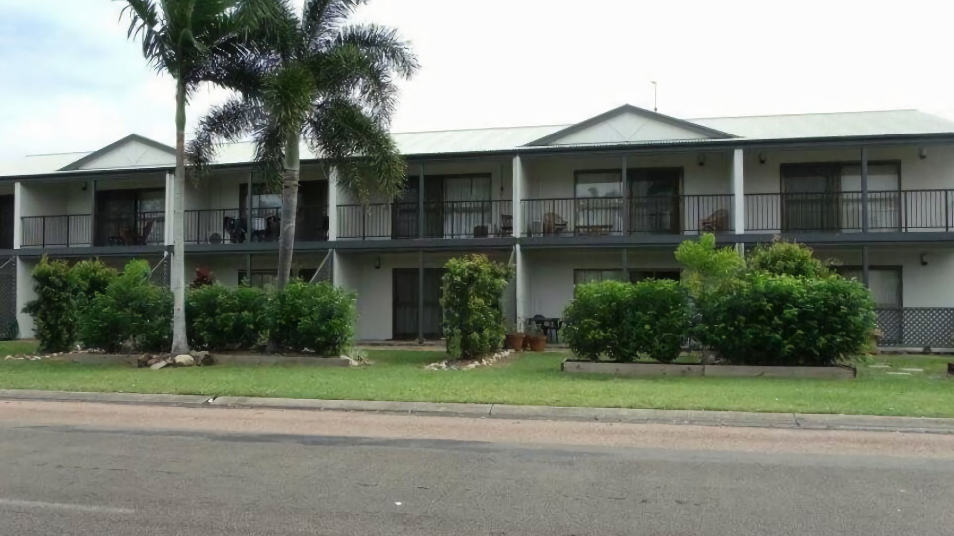 A multi-story building with balconies, a grassy lawn, and a palm tree.