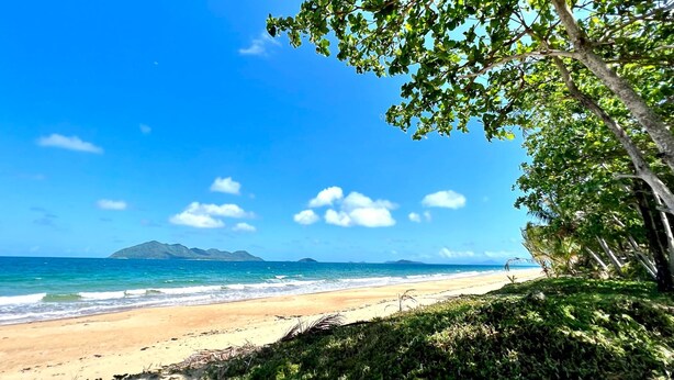 A beach with clear skies, ocean waves, and distant mountains.