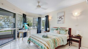 Un dormitorio con cama, escritorio, silla, mesa, ventilador de techo y vistas al exterior.