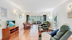 Una sala de estar con televisor, muebles de mimbre, un sofá y vistas al exterior.