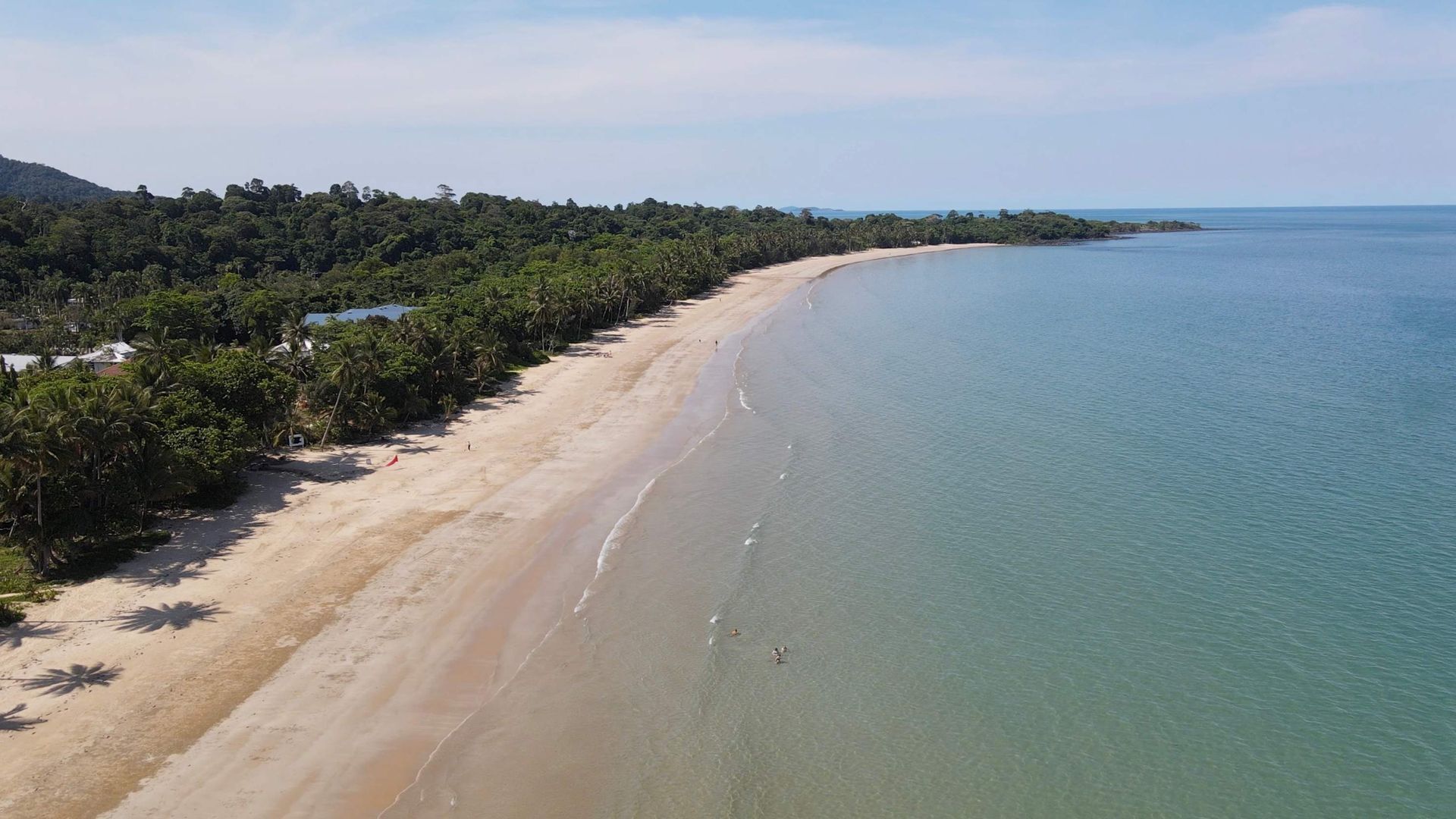 A beach with clear water, a sandy shore, and dense vegetation along the coastline.
