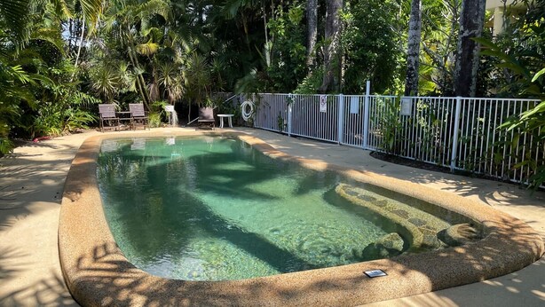 A clear swimming pool surrounded by a white fence, with lounge chairs and a table nearby. - Liana 4 Beach Lovers All at your finger tips (Mission Beach)