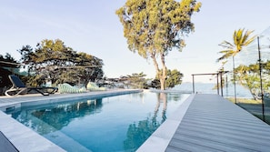 Una piscina infinita con sillas de descanso y una terraza de madera.