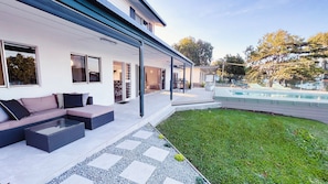 Un espacio exterior moderno con piscina, un patio cubierto y una zona de estar con cojines.