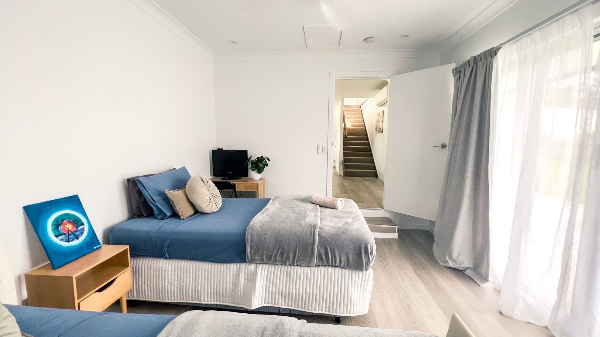A bedroom with a bed, a TV, a painting, and a staircase leading to another room.