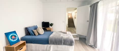 A bedroom with a bed, a TV, a painting, and a staircase leading to another room.