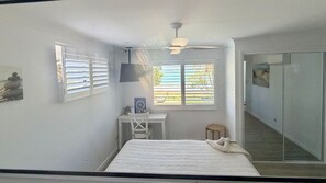 A bedroom with a bed, a desk, a chair, a ceiling fan, and a window with blinds.
