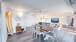 Una sala moderna con comedor, un televisor de pantalla plana grande y una decoración con tabla de surf.