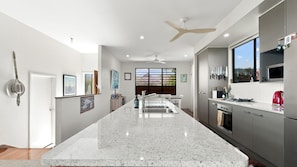 A modern kitchen with a central island, stainless steel appliances, and a large window providing natural light. - The Rise Dunk Island views and ocean breeze (Mission Beach)