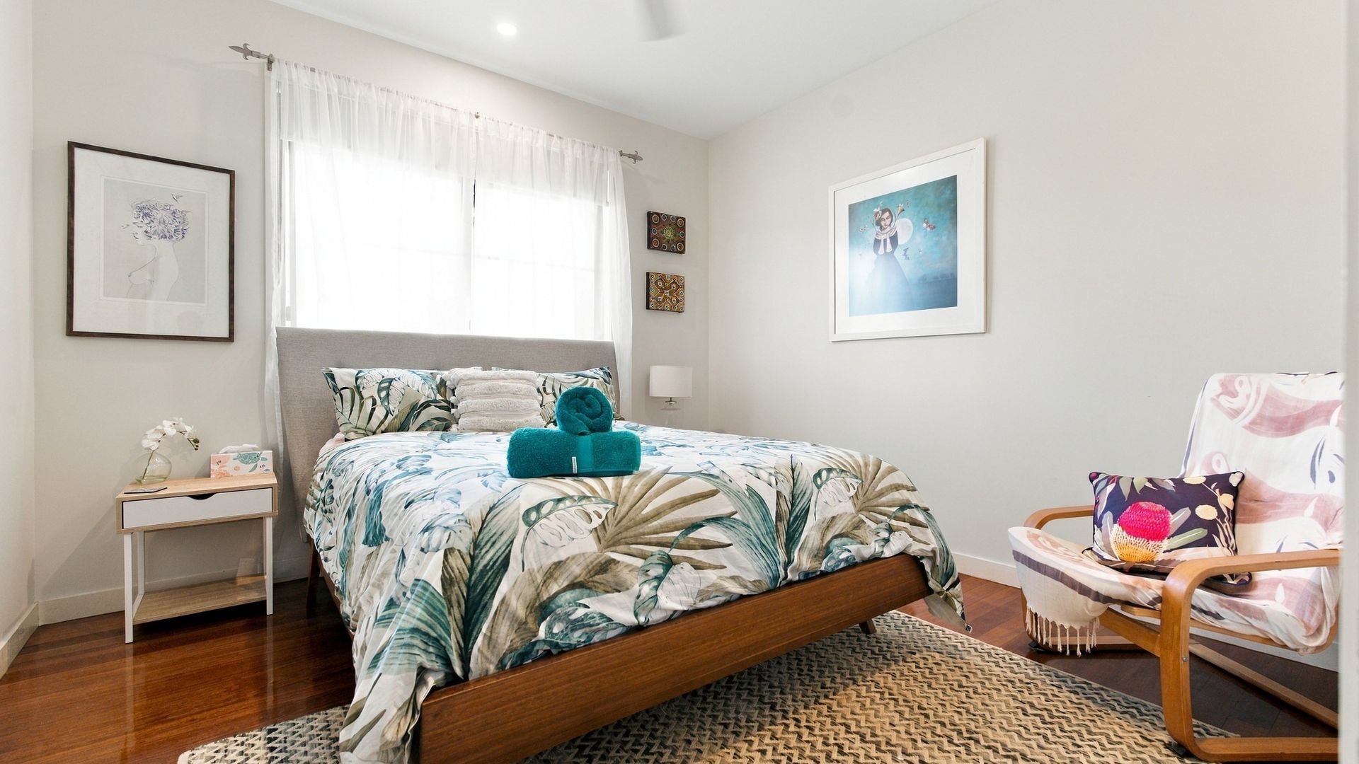 Une chambre à coucher avec un lit, une table de chevet, une chaise et des œuvres d’art accrochées aux murs.