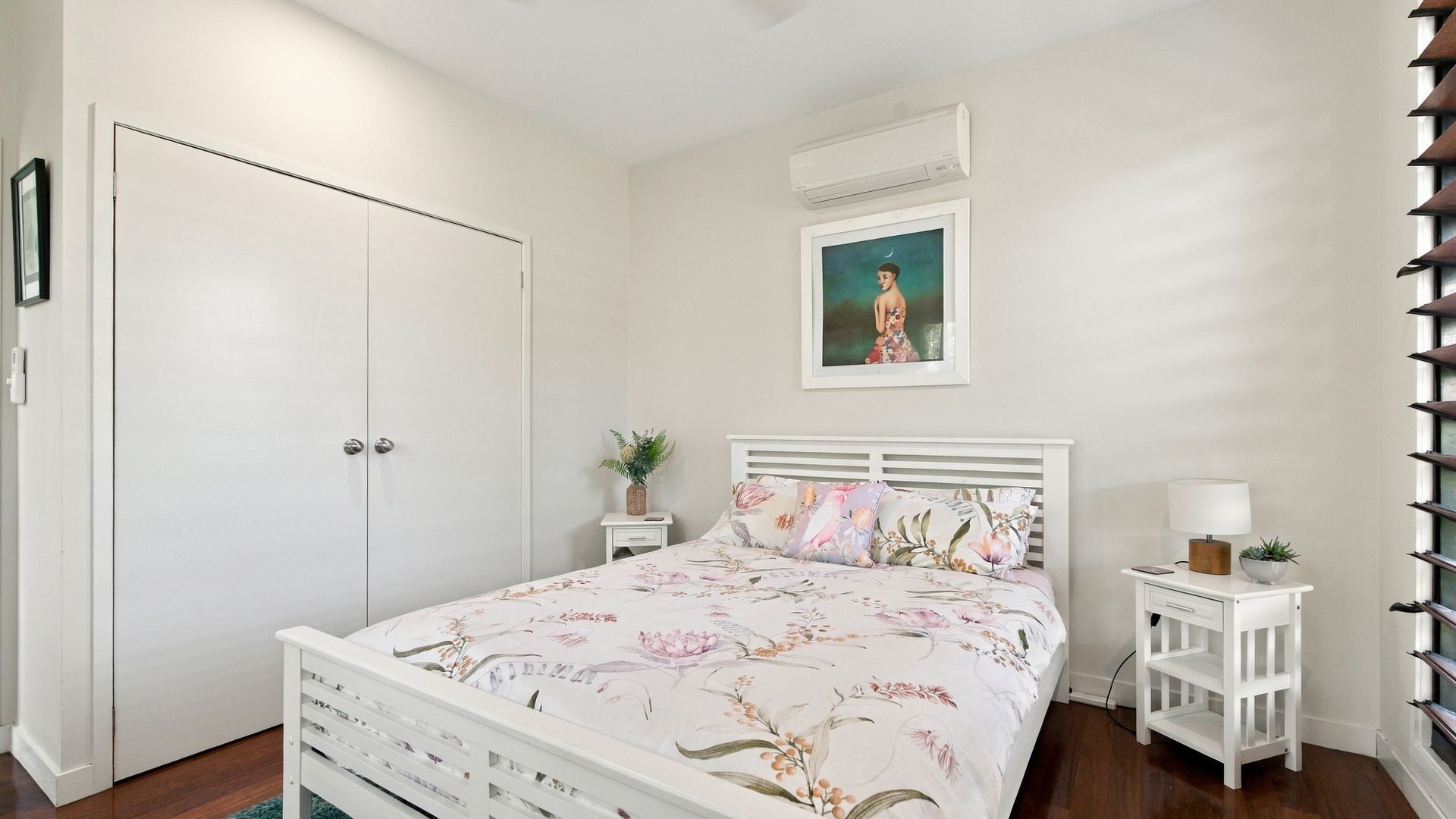 A bedroom with a bed, a nightstand, a wall-mounted air conditioner, and a door.