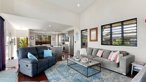 A modern living room with a grey sofa, a coffee table, and a dining area with a kitchen in the background.