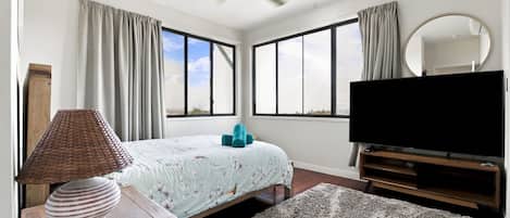 Un dormitorio con cama, televisión, espejo y ventana.