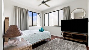 A bedroom with a bed, a television, a mirror, and a window.