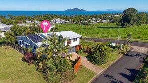 A modern house with solar panels, surrounded by lush greenery and a view of the ocean. - The Rise Dunk Island views and ocean breeze (Mission Beach)