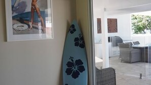 A room with a surfboard, a framed picture, and a view of an outdoor seating area. - Solace Dream Beachfront Escape (South Mission Beach)