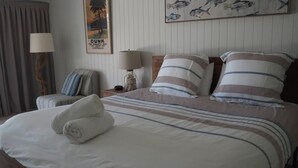 A hotel room with a bed, pillows, a nightstand, a lamp, a chair, a poster, and curtains. - Solace Dream Beachfront Escape (South Mission Beach)