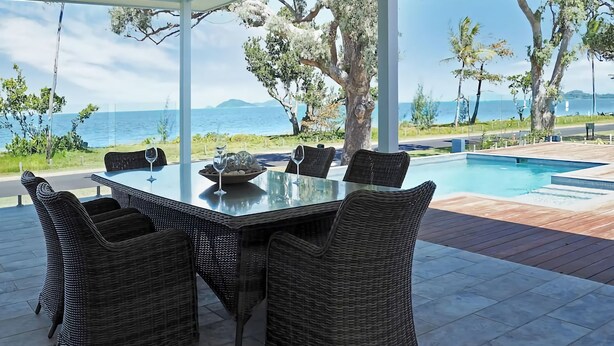 An outdoor dining area with wicker chairs and a glass table, overlooking a pool and the sea. - Solace Dream Beachfront Escape (South Mission Beach)
