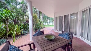 Une terrasse avec une table et des chaises en bois, entourée d’une végétation luxuriante et offrant une vue sur la mer.