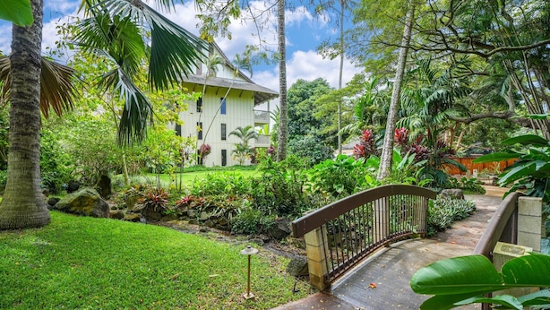 A lush garden with a stone bridge, a white building with multiple windows, and a variety of tropical plants. - South Kauai Tranquil Retreat w/ AC in Poipu (Koloa)