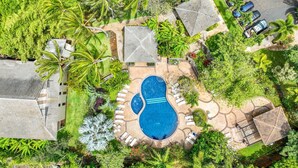 An aerial view of a residential area with a swimming pool, surrounded by lush greenery and a few houses. - South Kauai Tranquil Retreat w/ AC in Poipu (Koloa)