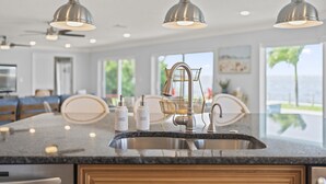 A kitchen with a large island, stainless steel appliances, and pendant lighting.
