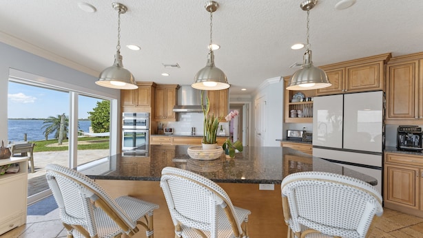 A spacious kitchen with a large island, three pendant lights, wooden cabinets, and a view of the ocean.