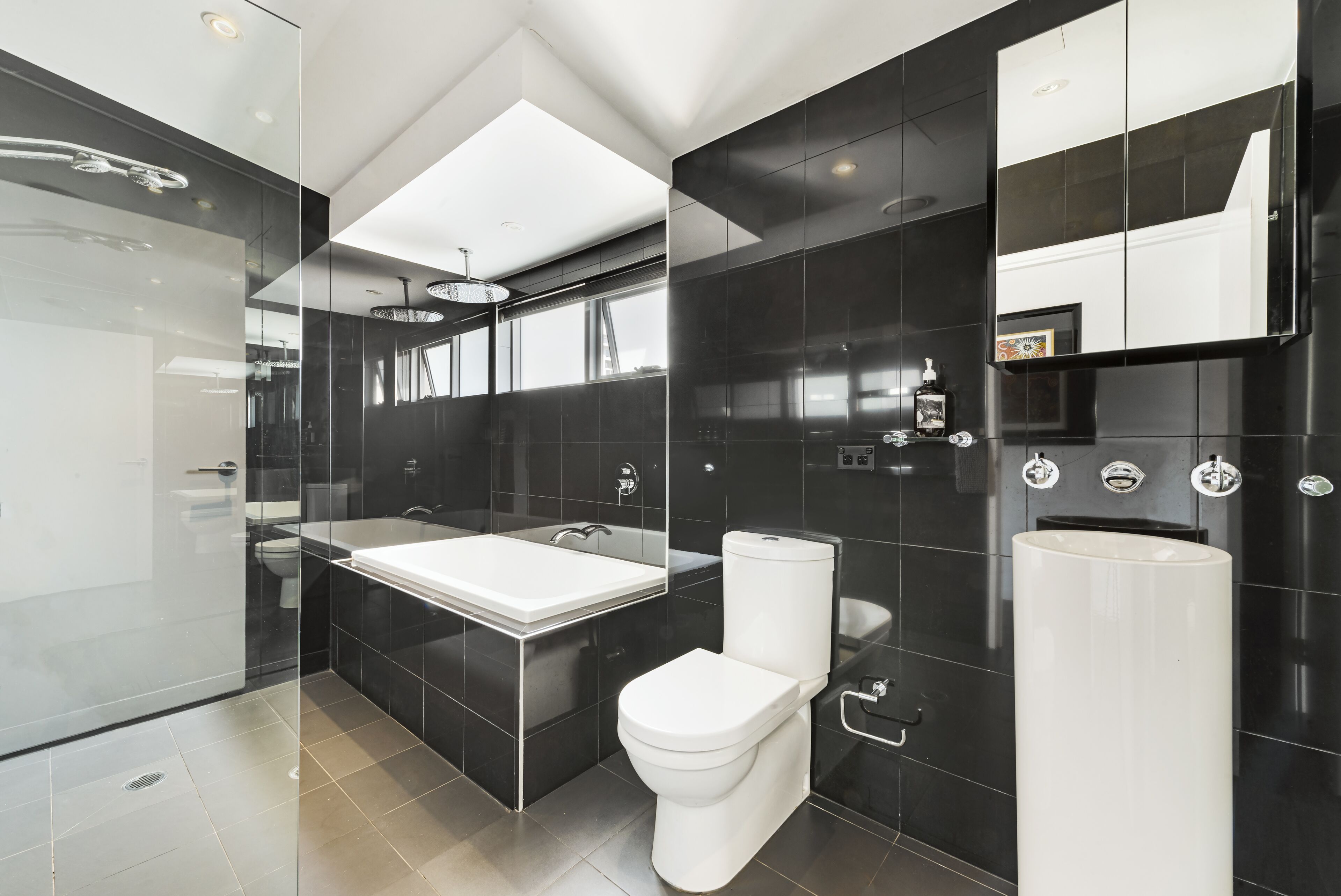 A modern bathroom with a glass shower enclosure, a white toilet, a large sink, and a tall pedestal sink.