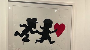 Une œuvre d’art encadrée représentant deux personnages tenant un cœur, une bougie turquoise et une statue de Bouddha sur une étagère.