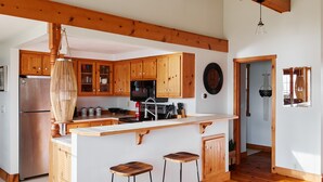 Une cuisine spacieuse avec des poutres en bois, un îlot central doté de tabourets et un réfrigérateur en acier inoxydable.