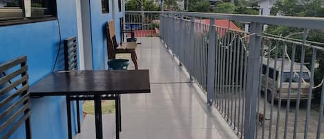 Un balcón con mesa y sillas, un muro azul y vistas a una zona residencial con casas y un coche.